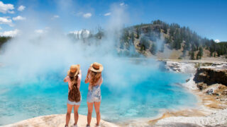 Girls relaxing and enjoying beautiful view of gazer on vacation hiking trip. Friends on hiking trip. Excelsior Geyser from the Midway Basin in Yellowstone National Park. Wyoming, USA