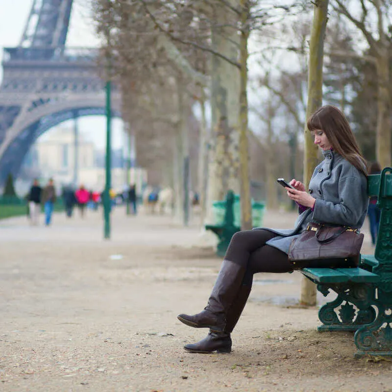 Young Woman Looking At Her Phone On Near Eiffel Tower, Paris, France