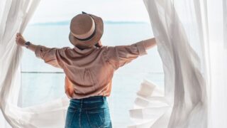 Woman opening curtains in hotel room and looking at ocean