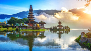 clouds, sun, and water surround a temple in Bali