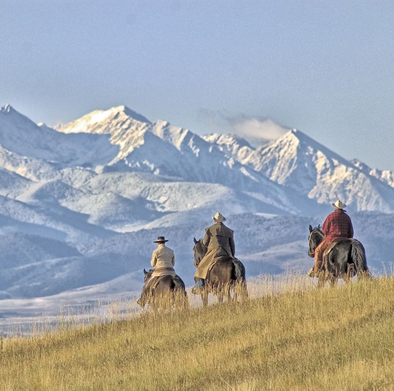 Cowboys on horses overlooking snow topped mountains