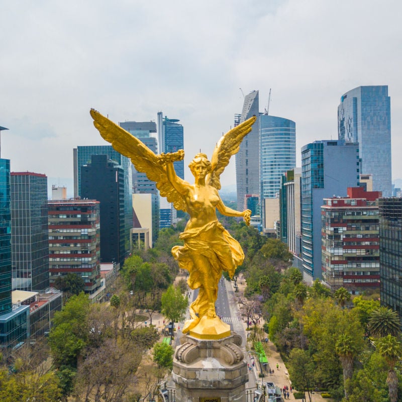 Frontal aerial view of the statue of the angel of independence on Reforma Avenue with Chapultepec forest.
