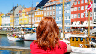 Woman enjoying the scenic view of Nyhavn pier. Colorful building facades with boats and yachts in the Old Town of Copenhagen, Denmark