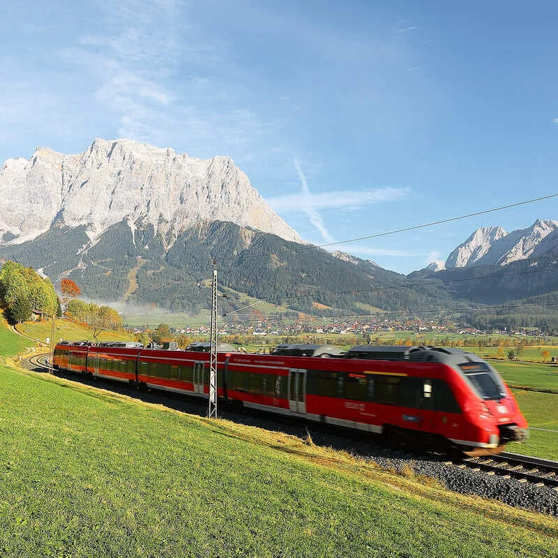 A Fast-Speed Austrian Railway Red Train Traveling Through The Green Landscape Of The Austrian Alps In Summer, Europe Train Travel