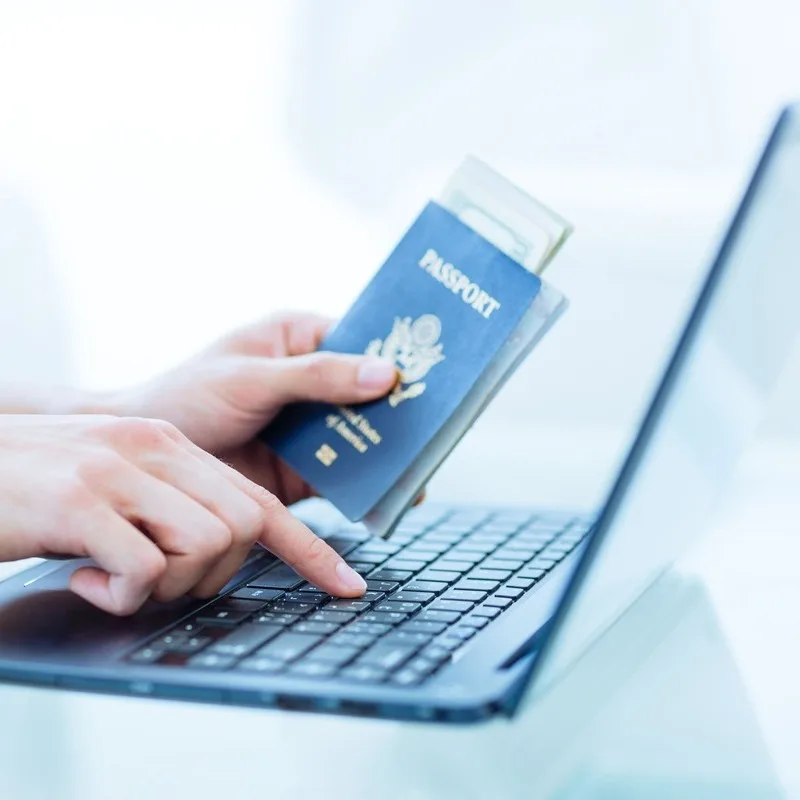 A Woman Holding Up A Passport As She Types On Her Computer