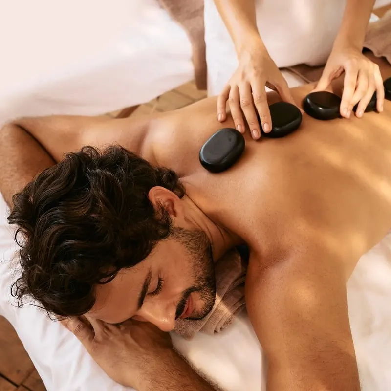 A Young Man Lying Topless On A Massage Table As He Undergoes Hot Stone Therapy Treatment, Spa, Relaxation And Wellness, Unspecified Location