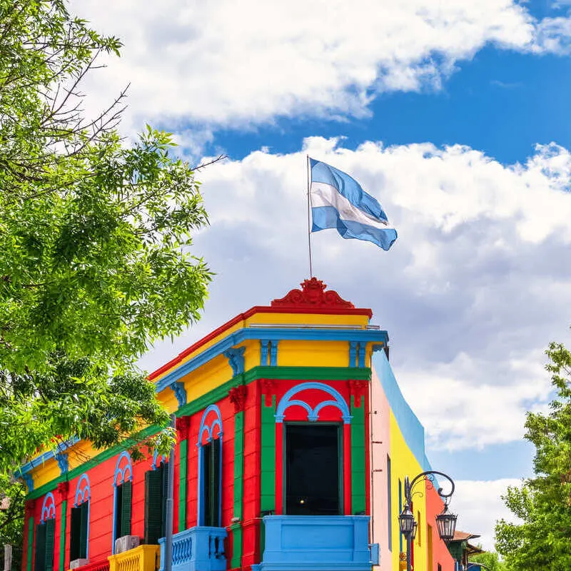 Argentinian Flag Flying Atop A Colorful Building In Buenos Aires, Argentina