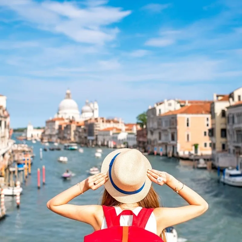 Female Tourist Holding Her Hat As She Stares At The Grand Canal In Venice, Northern Italy, Southern Europe