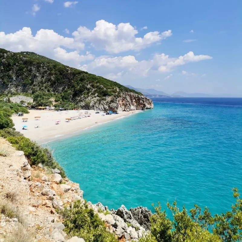 Gjipe beach with white sand, tourist tents and umbrellas, the turquoise Ionian sea hidden between mountains in canyon on a sunny day in Albania.