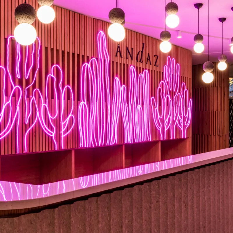 The Andaz Mexico City Condesa Reception Desk is backlit by purple neon lights of cacti and circular lights above. 