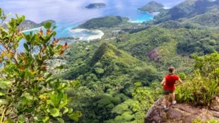 Young female traveller standing at the edge of the cliff at Morne Blanc View Point, overlooking Mahe Island coastline with lush tropical vegetation and crystal blue ocean, Seychelles copy