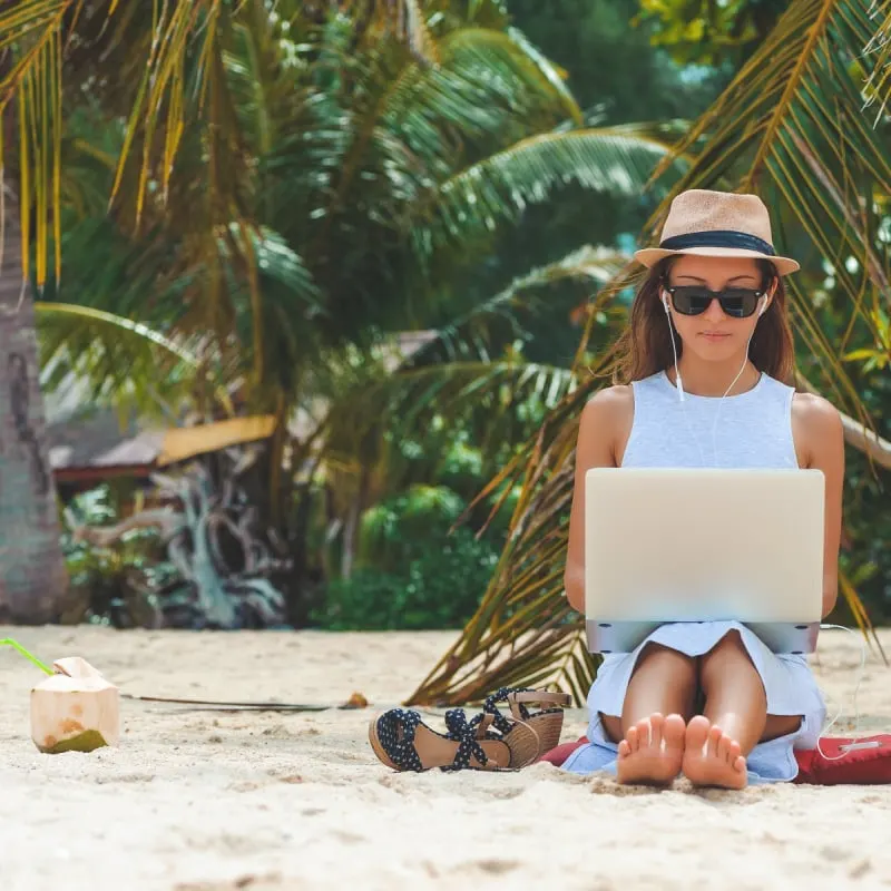 female digital nomad on beach with laptop