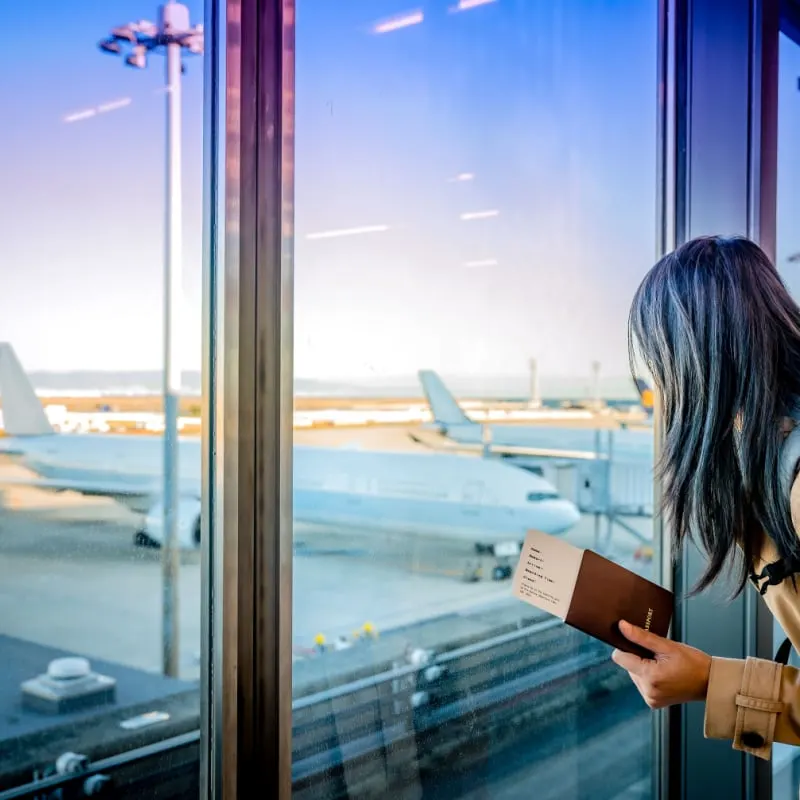 woman passenger with passport looks out at planes in airport