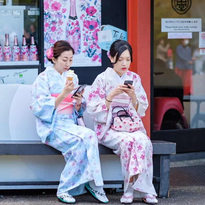 traditionally dressed Japanese women eating food on a bench