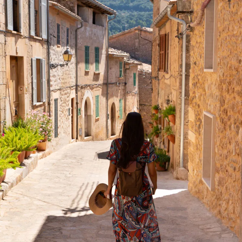 a woman walks down a street with stone buildings in Mallorca
