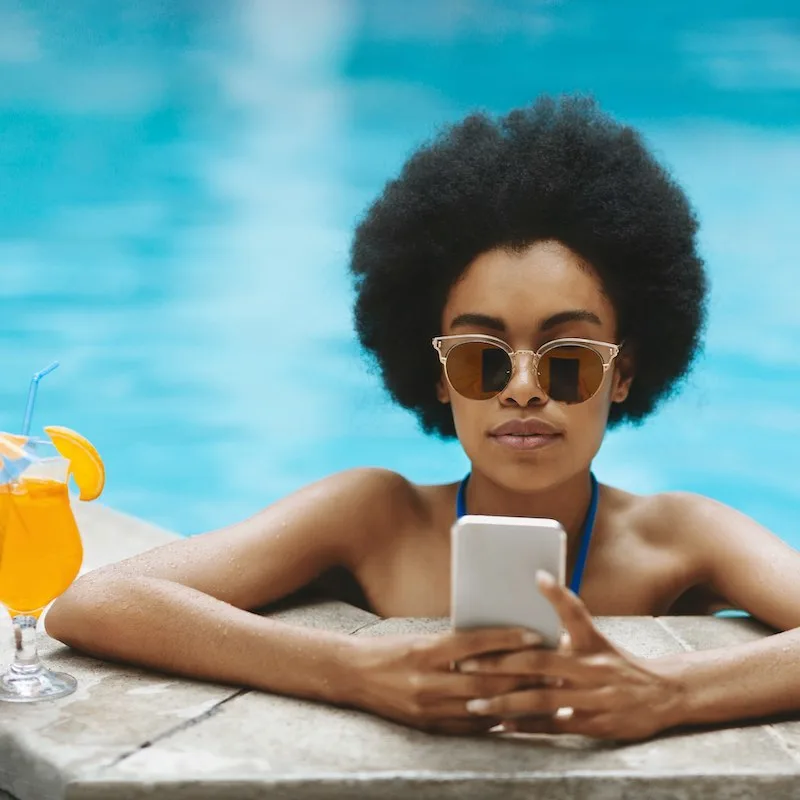 woman on vacation checks her phone by the pool