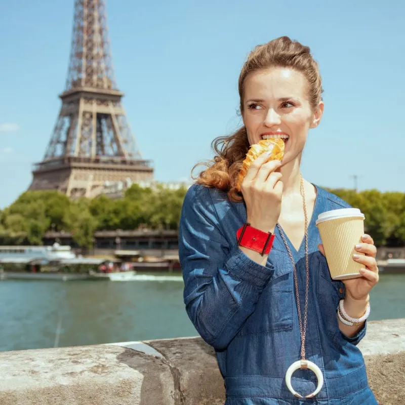 Woman eating a croissant next to the Eiffel Tower