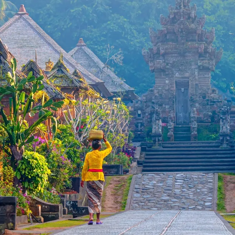 Woman carrying basket over her head walking towards a temple in Bali