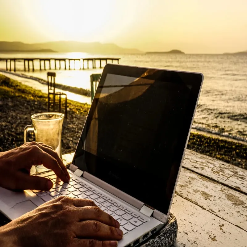 Working on laptop on beach on wooden table at sunset