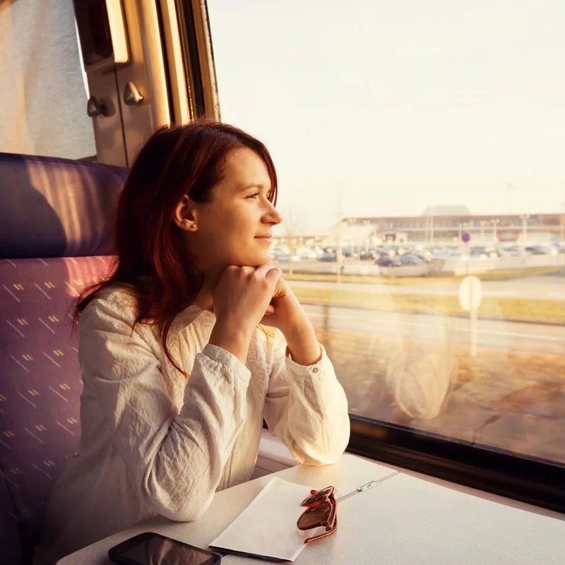 Young Woman Looking Happy Looking Out The Window As She Rides A Train In An Unspecified Location